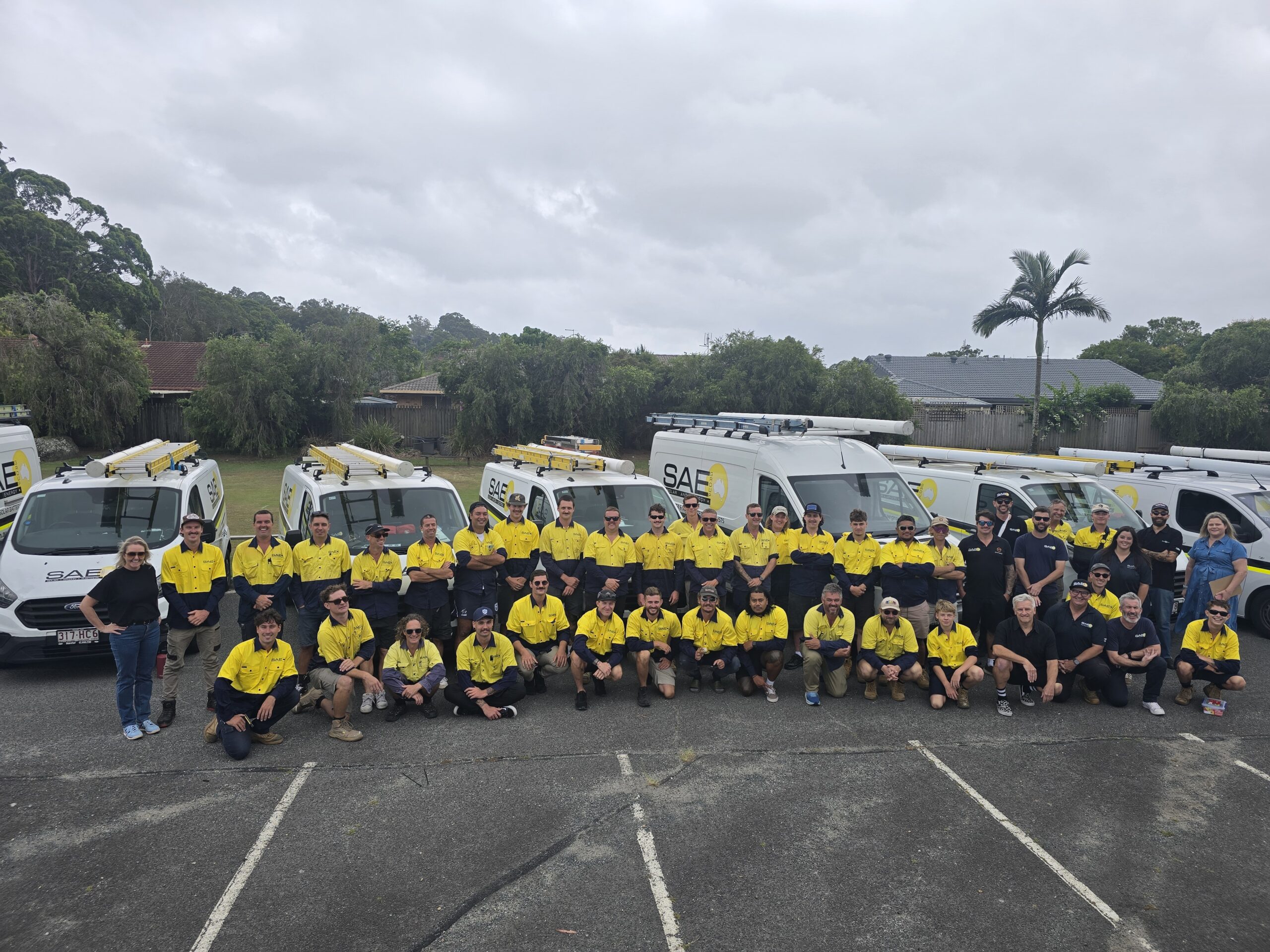 SAE Group team standing and kneeling in front of company service vehicles