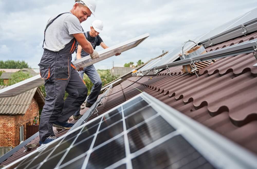  two male technicians on roof carrying solar panel for installation